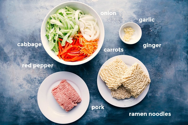 Assortment of ingredients for egg roll noodle recipe, including cabbage, red pepper, onion, carrots, ramen noodles, ground pork, garlic, and ginger.