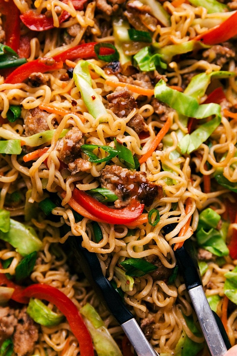 Up-close finished shot of pork Egg Roll Noodles with tongs holding a serving amount.