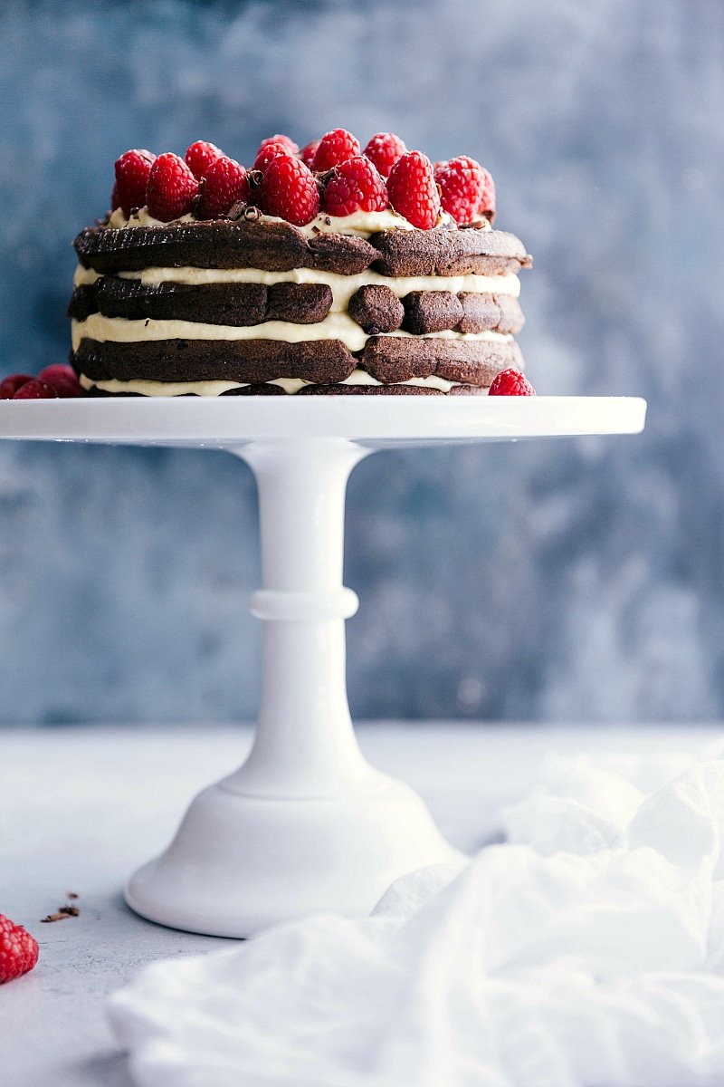 Waffle cake displayed on a cake stand, adorned with fresh raspberries on top.