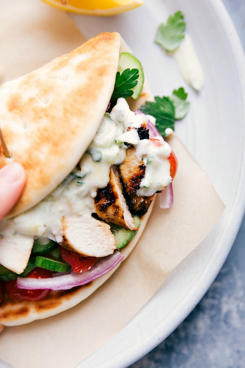 A chicken gyro wrapped in a soft pita, filled with seasoned chicken, fresh vegetables, and tzatziki sauce spilling out the sides, prepared to be eaten.