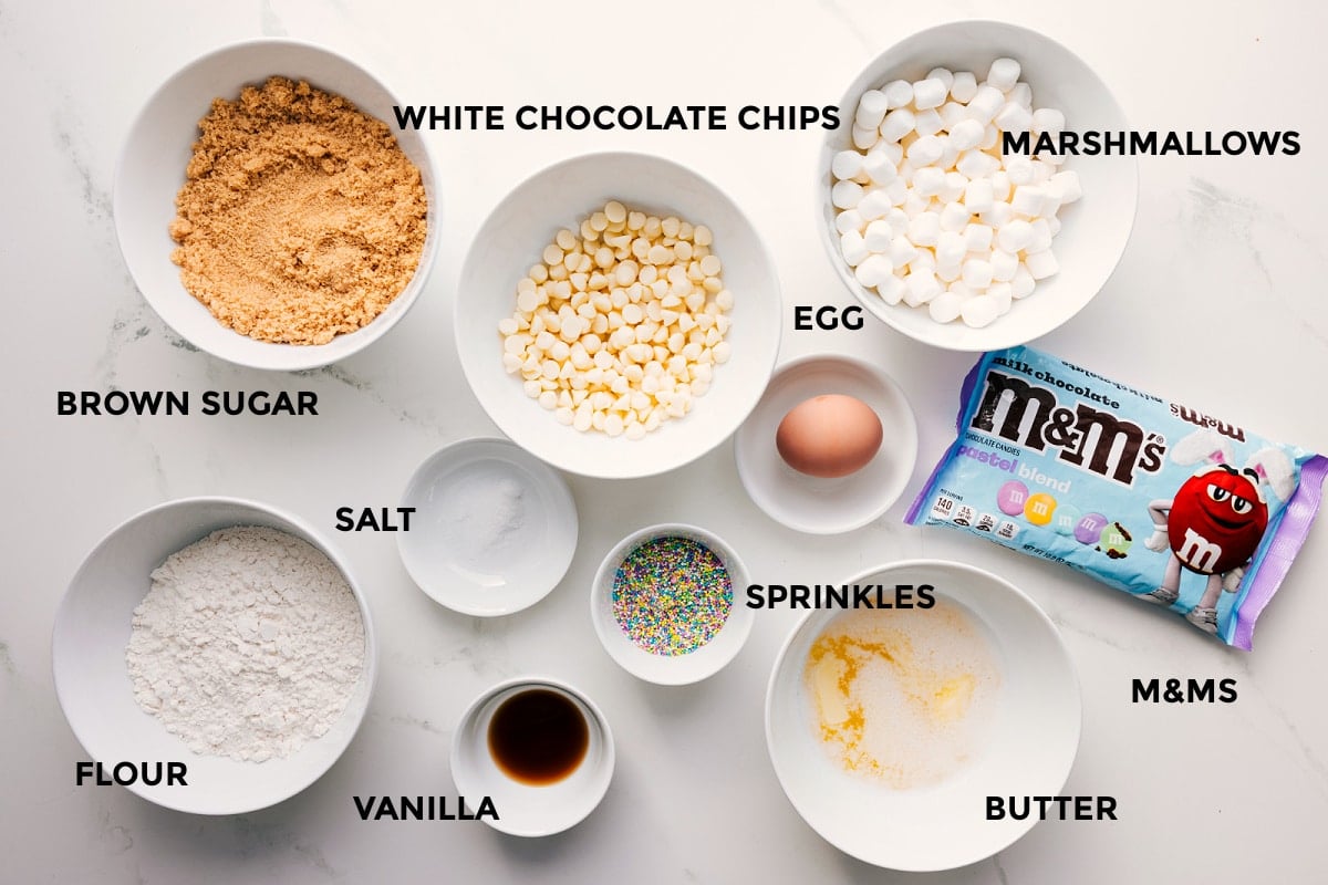 All the ingredients in this recipe prepped out for easy assembly including the brown sugar, flour, vanilla, salt, white chocolate chips, marshmallows, egg, M&Ms, butter, and sprinkles.