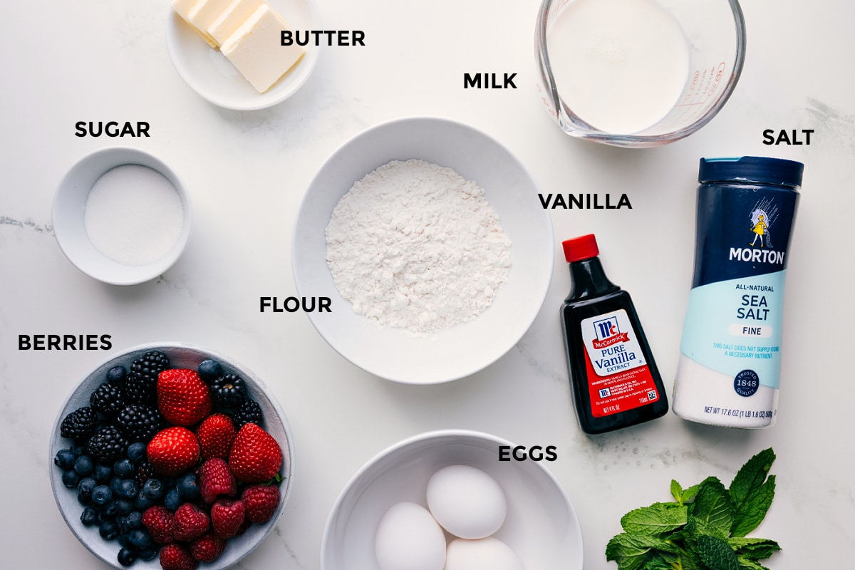 All the ingredients for this recipe prepped and ready for easy assembly, including butter, milk, salt, vanilla, flour, sugar, berries, and eggs.