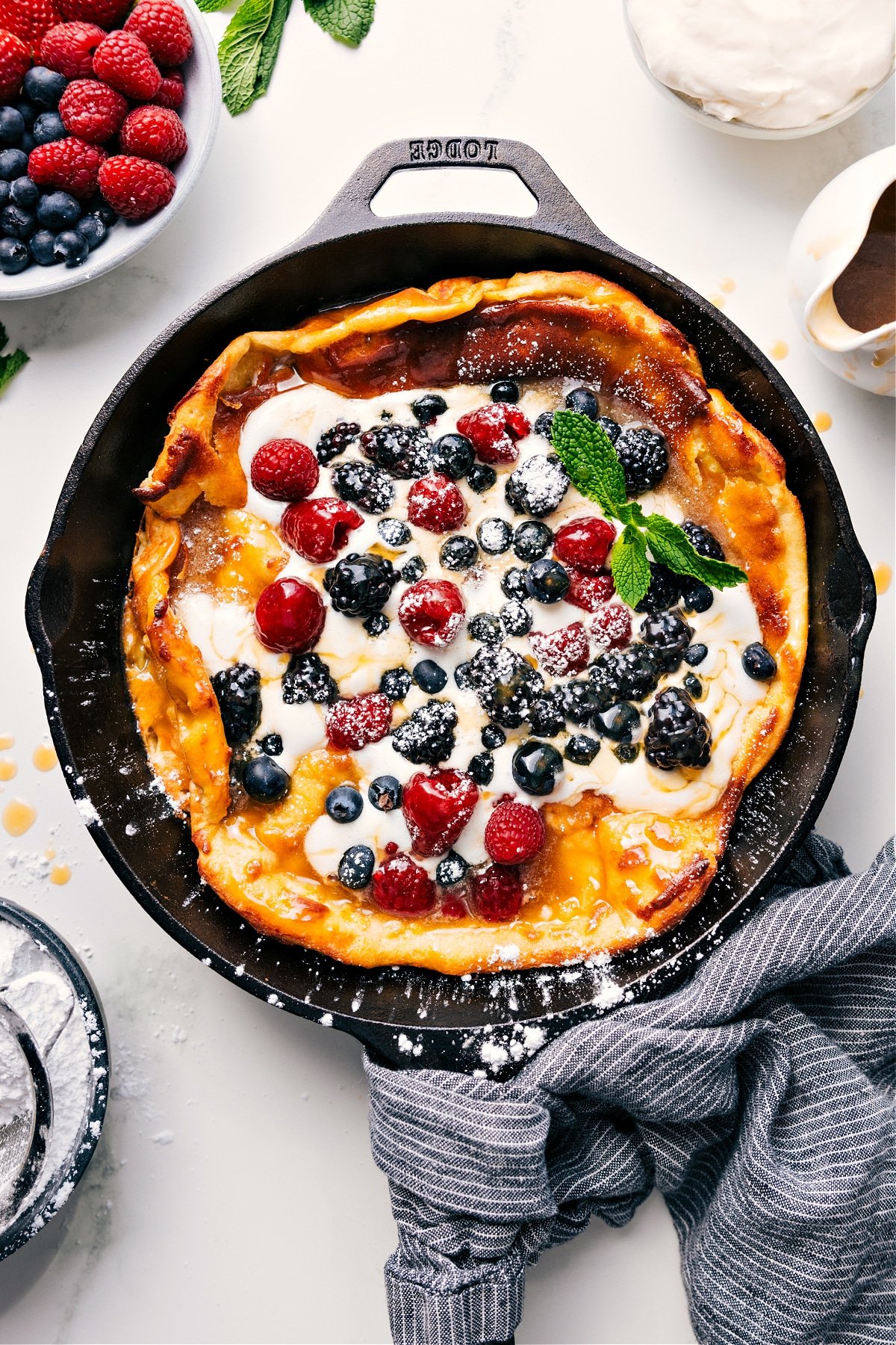 The Best Dutch Baby Recipe Dutch Baby skillet topped with fresh whipped cream, berries, and syrup.