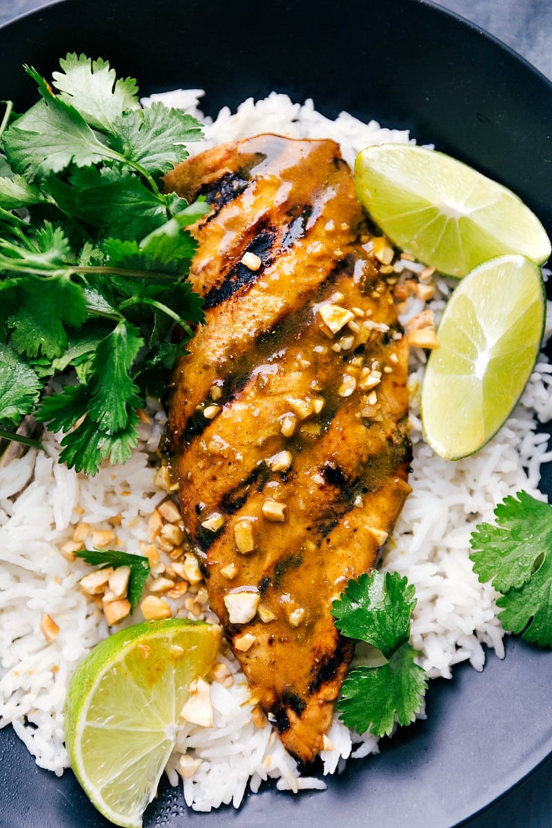 Up-close overhead image of Grilled Curry Chicken over coconut rice with fresh lime wedges and cilantro on the side.