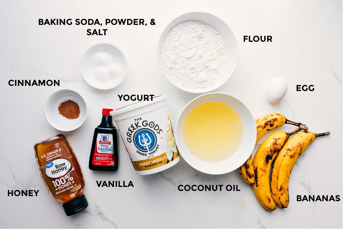 All the ingredients prepped for easy assembly, including flour, eggs, fruit, coconut oil, yogurt, baking soda, powder, salt, cinnamon, vanilla, and honey.