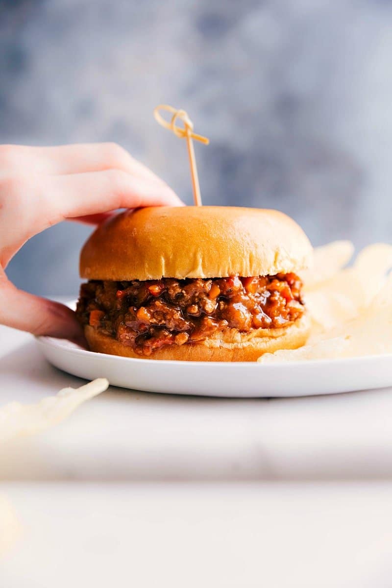 View of Turkey Sloppy Joes on a plate with a hand holding the sandwich.