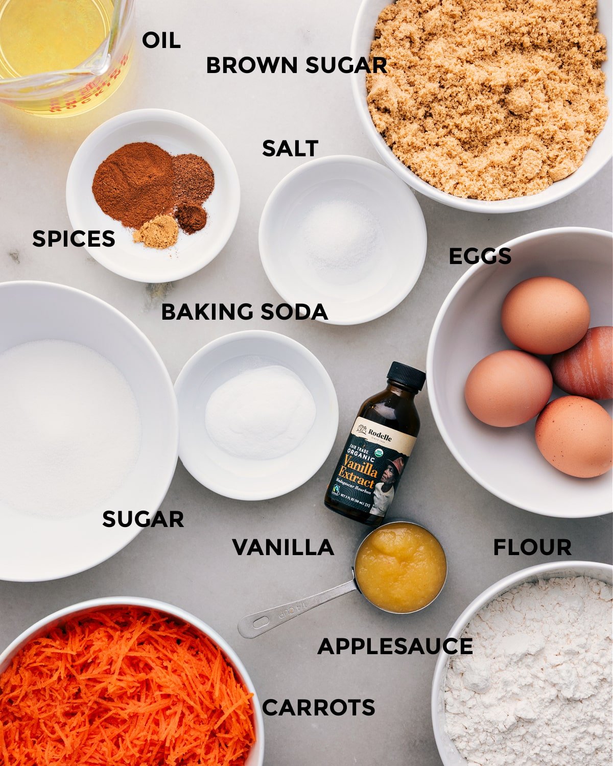 I’ve prepped all the ingredients for easy assembly—oil, brown sugar, eggs, salt, spices, baking soda, vanilla, sugar, flour, applesauce, and carrots.