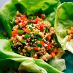 Chicken lettuce wrap filled with meat and veggie mixture, garnished and ready to eat.