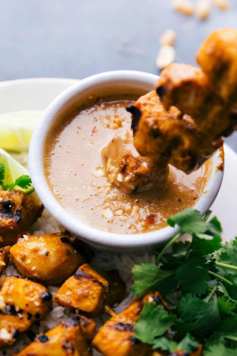 Photo of a Peanut Sauce Chicken skewer being dipped into peanut sauce.