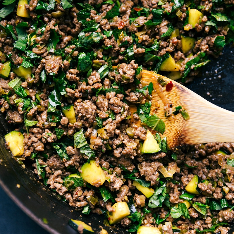 Wooden spoon serving a portion from a pan of the finished larb beef dish.