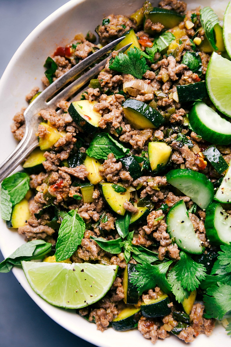 Shot of a plate full of Beef Larb with a fork to the side, and lime and herb garnishes.