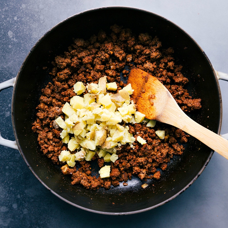 Diced potatoes being mixed into the sautéed beef.