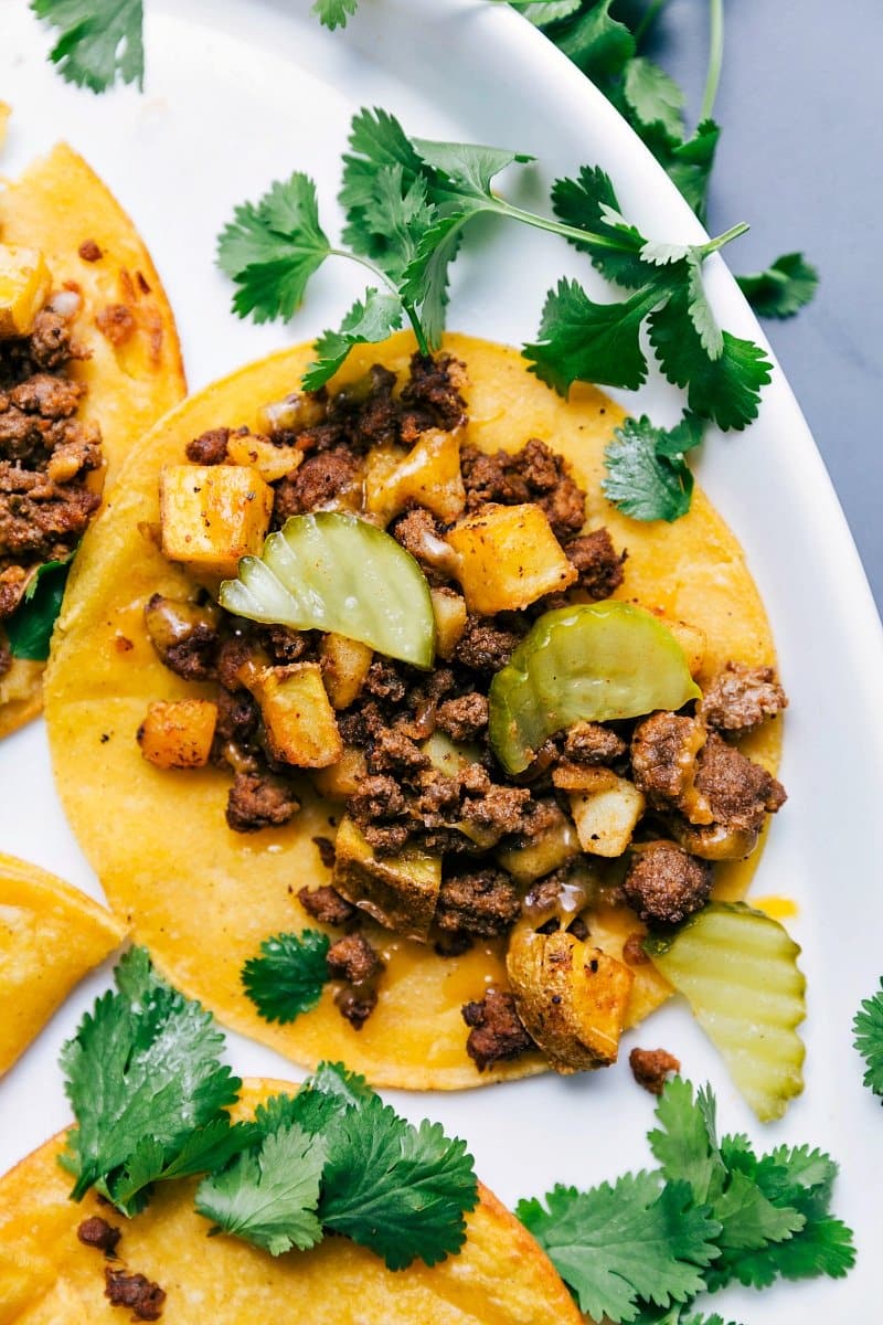 Beef and potato tacos with pickles on top and cilantro on the side.