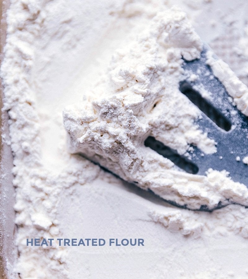 Flour spread on a baking sheet being heat-treated in an oven, a crucial step to ensure the dough is safe to consume raw.