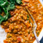 Savory lentil curry in a dish with a fork, accompanied by fresh cilantro and a side of rice.