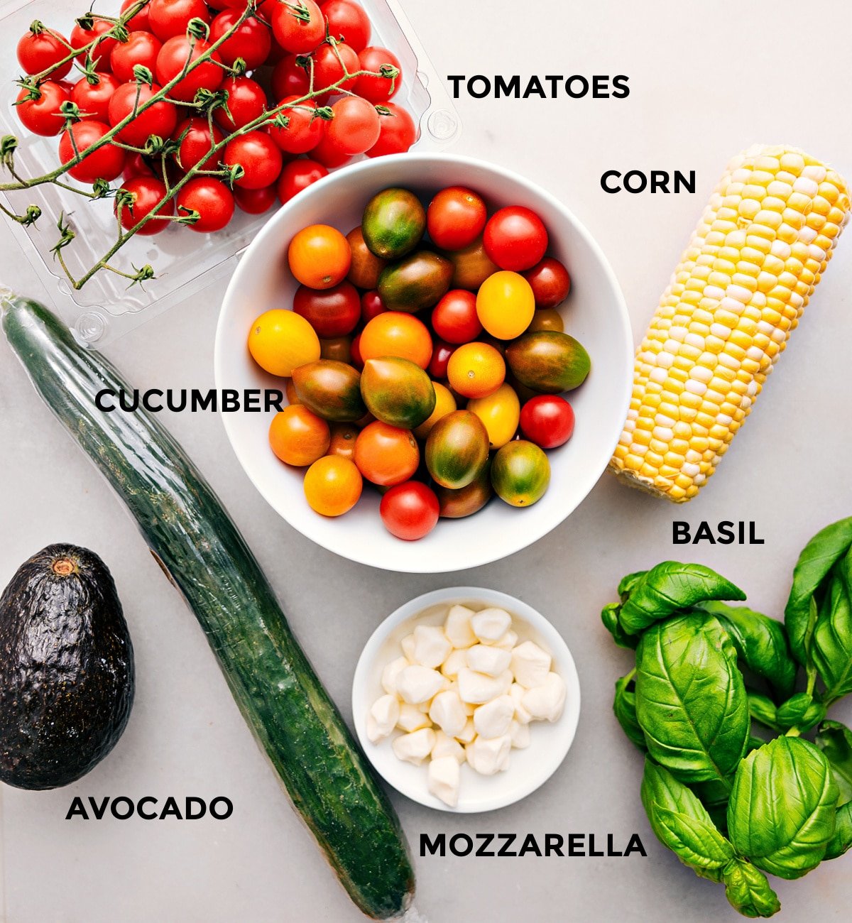 All the ingredients for this recipe are prepped for easy assembly, including the tomatoes, corn, cucumber, basil, mozzarella, and avocado.