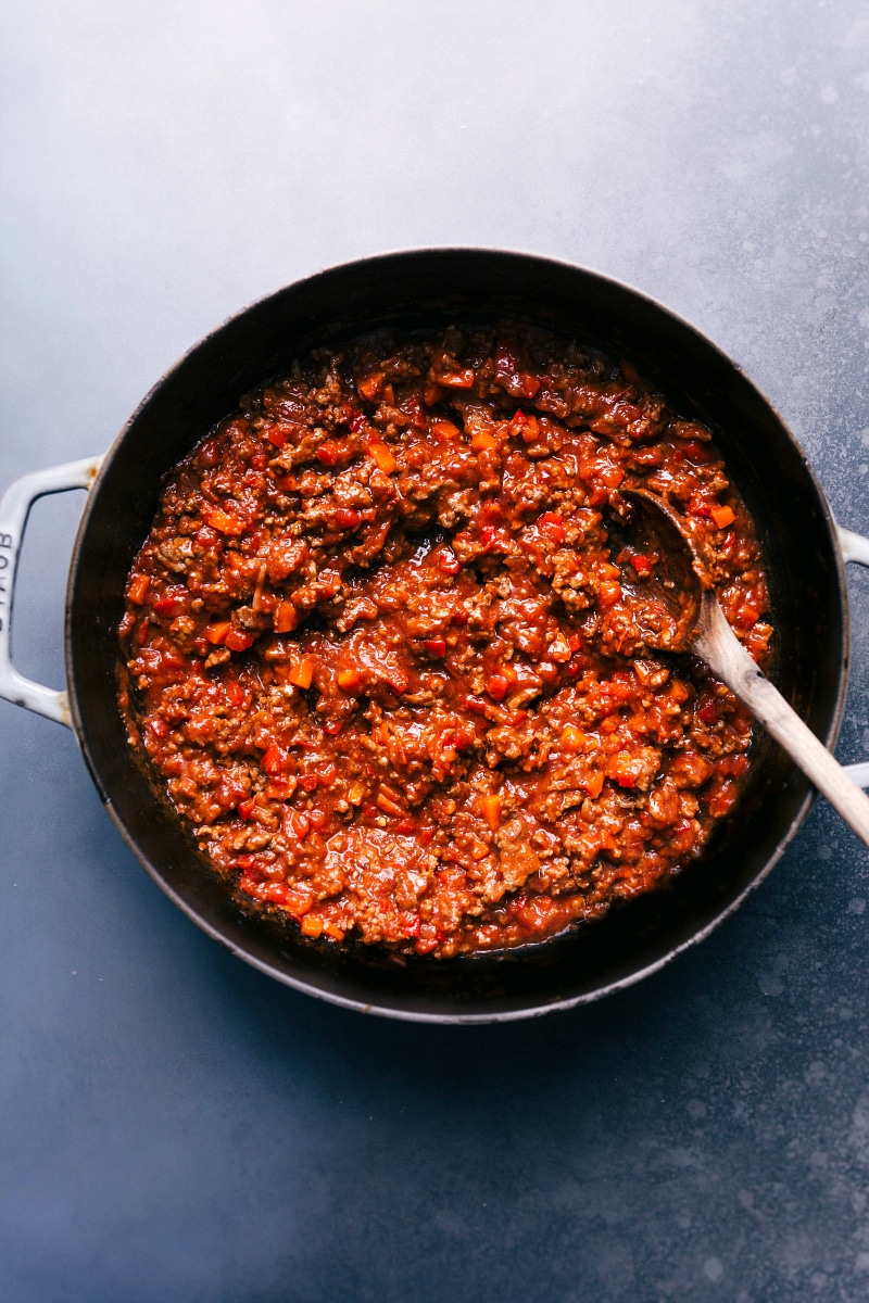 Thick, savory Sloppy Joes mixture simmering in a skillet, with a spoon for serving nestled inside.