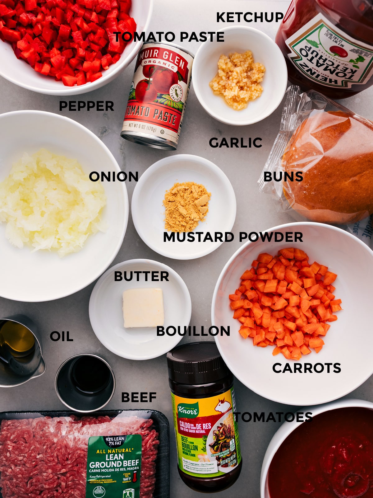 All the ingredients for this recipe—ketchup, pepper, tomato paste, buns, seasonings, onion, butter, bouillon, beef, and tomatoes—prepped and ready for easy assembly.