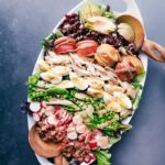 A generous serving platter heaped with a cobb salad masterpiece, boasting meats, fresh vegetables, fruit, and drizzled with creamy balsamic dressing.