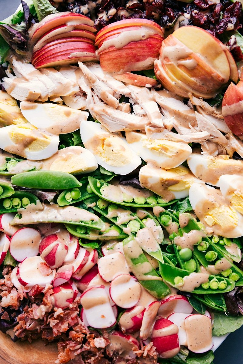 View of Creamy Balsamic Dressing with salad ingredients: apples, chicken, hard-boiled eggs, sugar snap peas, and radishes.