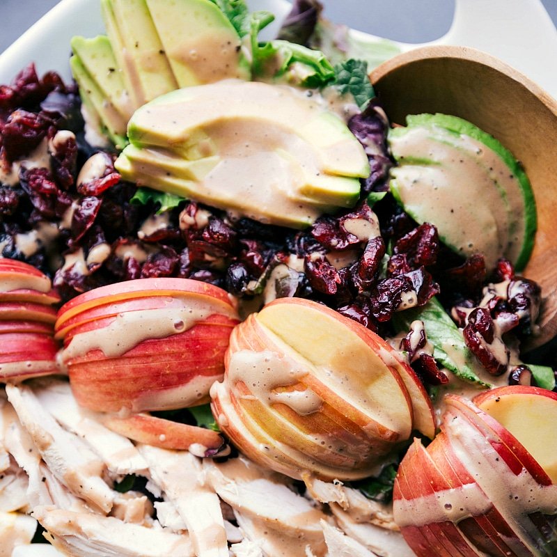 Close-up image of Creamy Balsamic Dressing coating salad ingredients: avocado, Fuji apple, sliced chicken, dried cranberries, and lettuce.