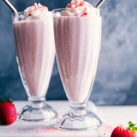 Two Strawberry Milkshakes with whipped cream on top and straw in them.