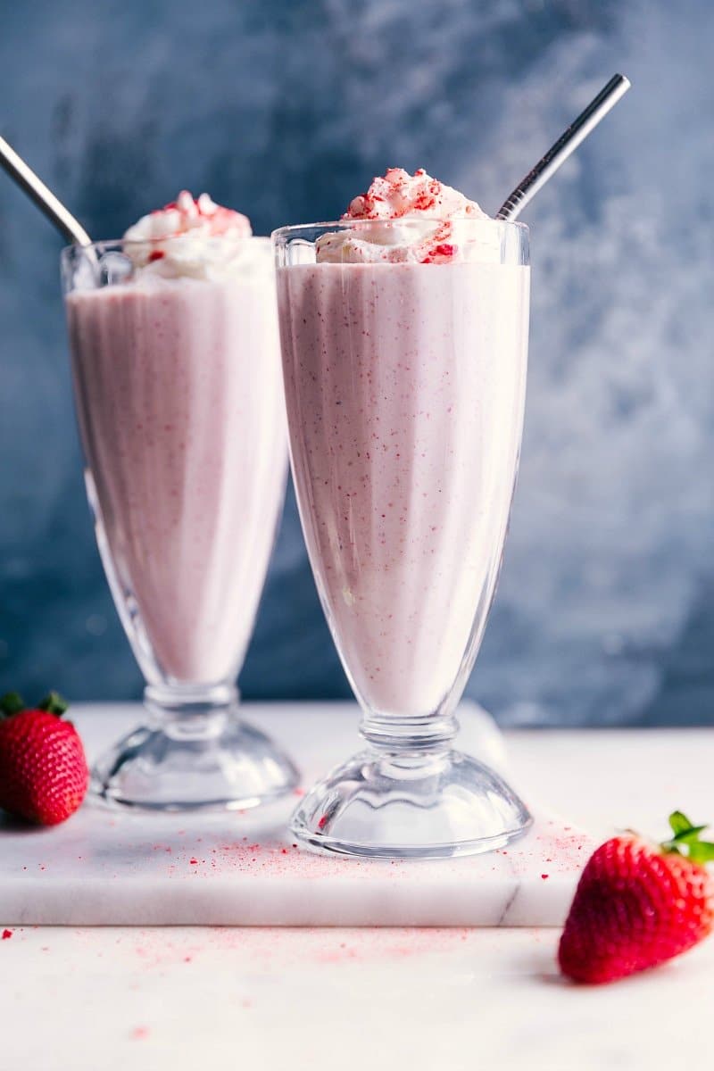 Two Strawberry Milkshakes with whipped cream on top and straw in them.