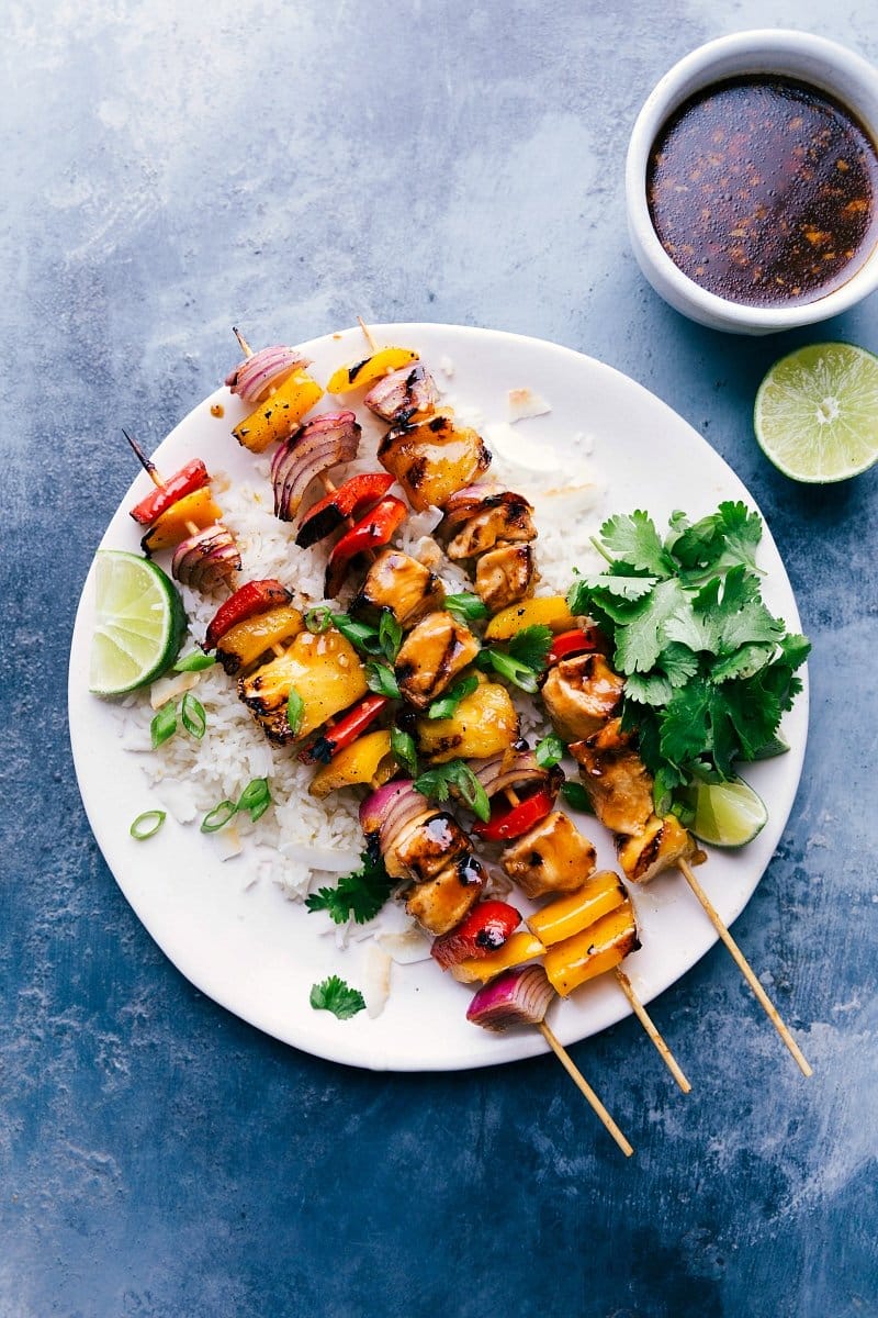 Overhead image of Teriyaki Chicken Skewers on a bed of rice, with lime, cilantro and toasted coconut.