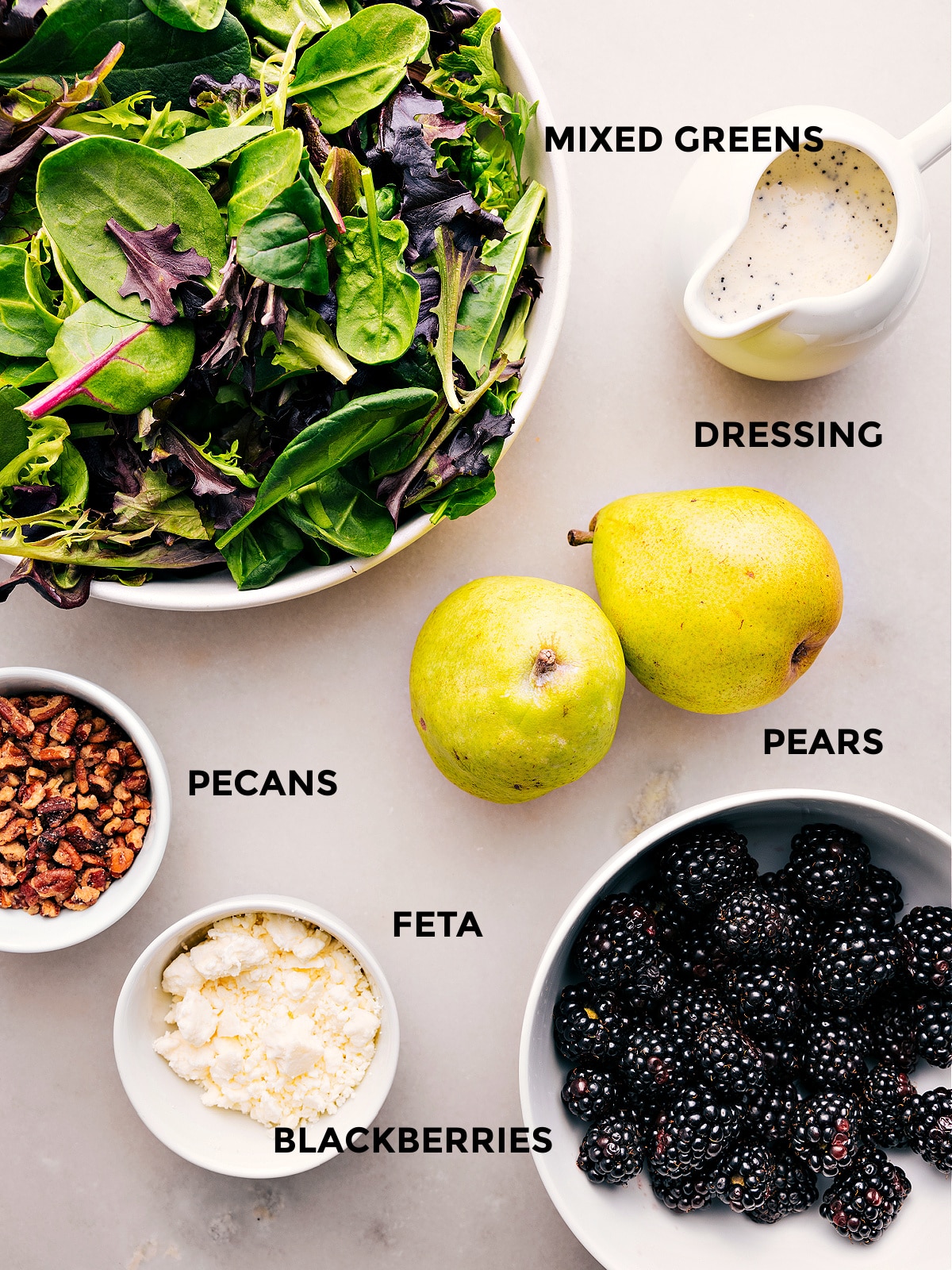 All the ingredients in this recipe are prepped for easy assembly, including the dressing, greens, pears, blackberries, feta, and pecans.