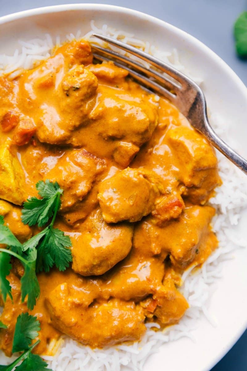 Plate full of butter chicken atop rice, ready for eating.