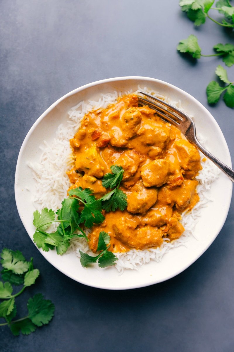 Image of a plate full of Butter Chicken on a bed of rice, garnished with cilantro.