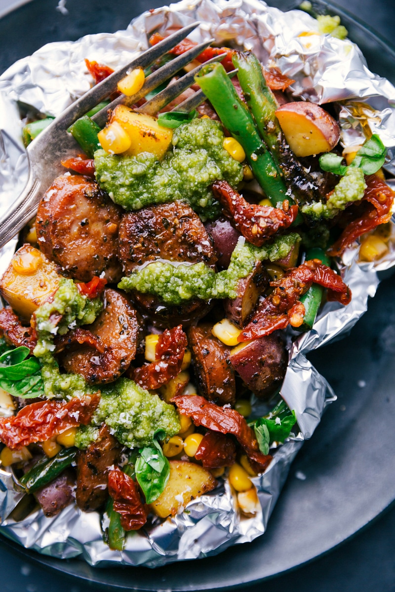 Up-close overhead image of the foil pack dinner with fresh pesto on top and a fork in it.