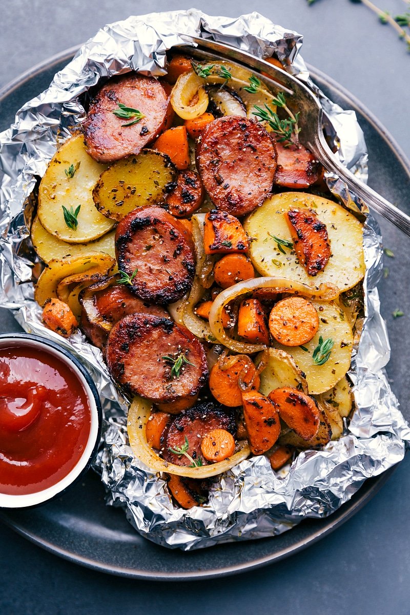 Hobo foil packets with meat and vegetables, served with ketchup.