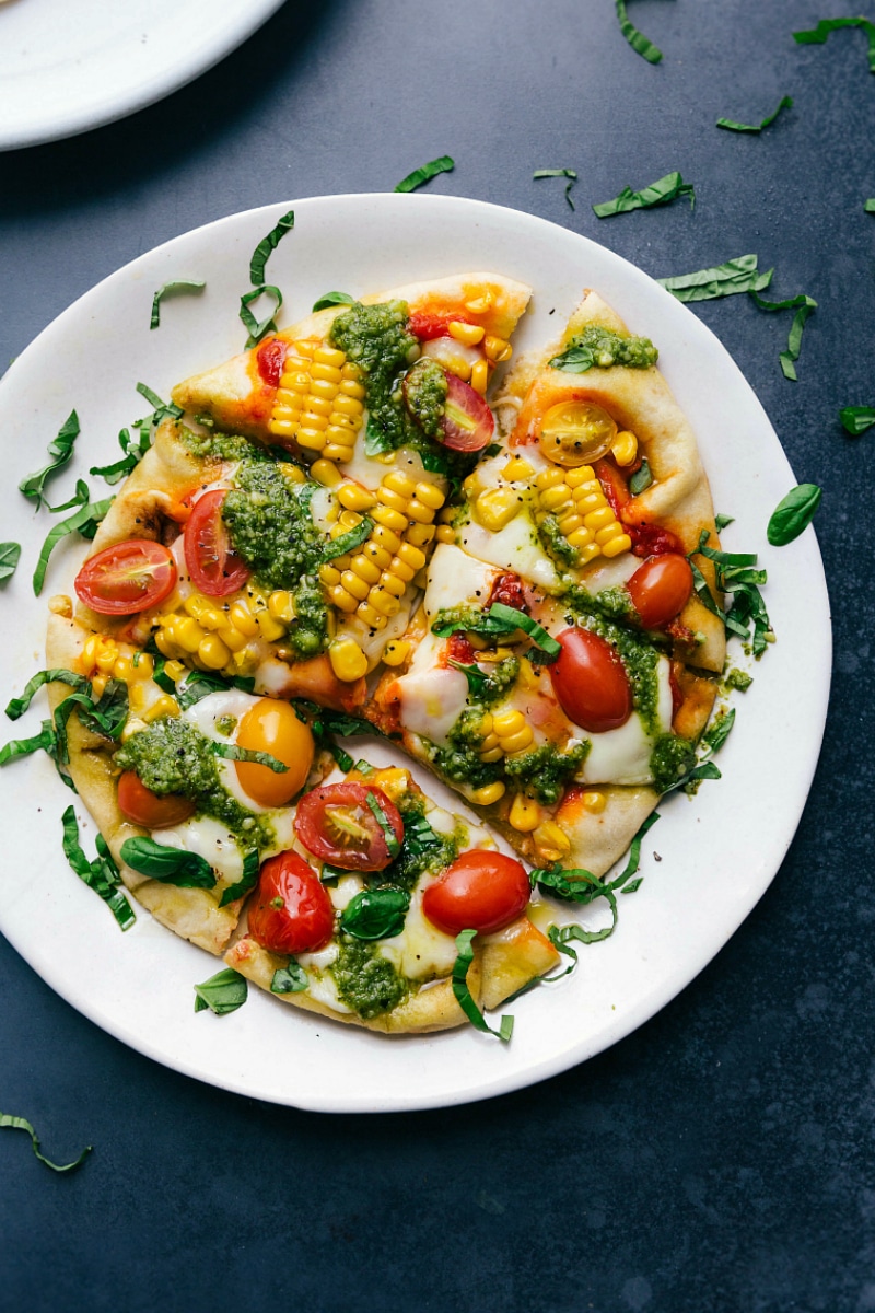 Baked pesto pizza with fresh vegetable toppings, sliced and ready to serve.