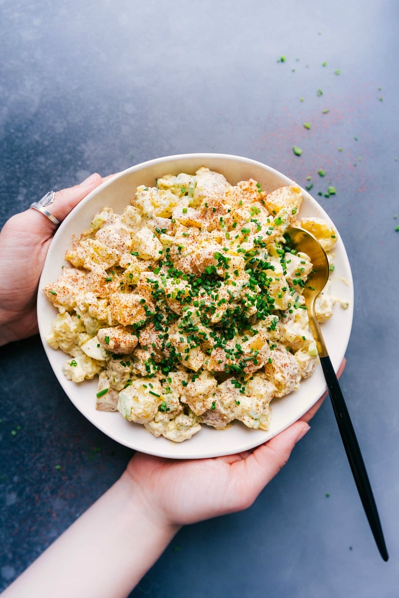 Large bowl of creamy potato salad recipe garnished with fresh herbs, ready to be savored.