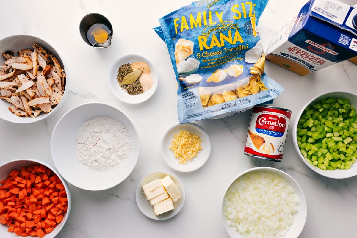 All the ingredients in this recipe prepped out for easy assembly including the chicken, onion, carrots, celery, butter, olive oil, flour, chicken broth, bouillon, tortellini, and evaporated milk.