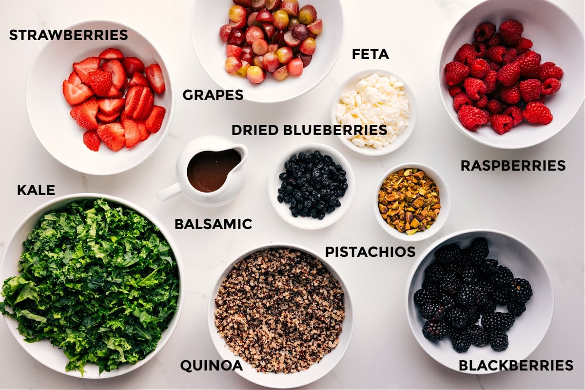 Ingredients In Kale Quinoa Salad All the ingredients in this recipe prepped out for easy assembly including the kale, strawberries, grapes, feta, balsamic, quinoa, feta, dried blueberries, pistachios, blackberries, and raspberries.