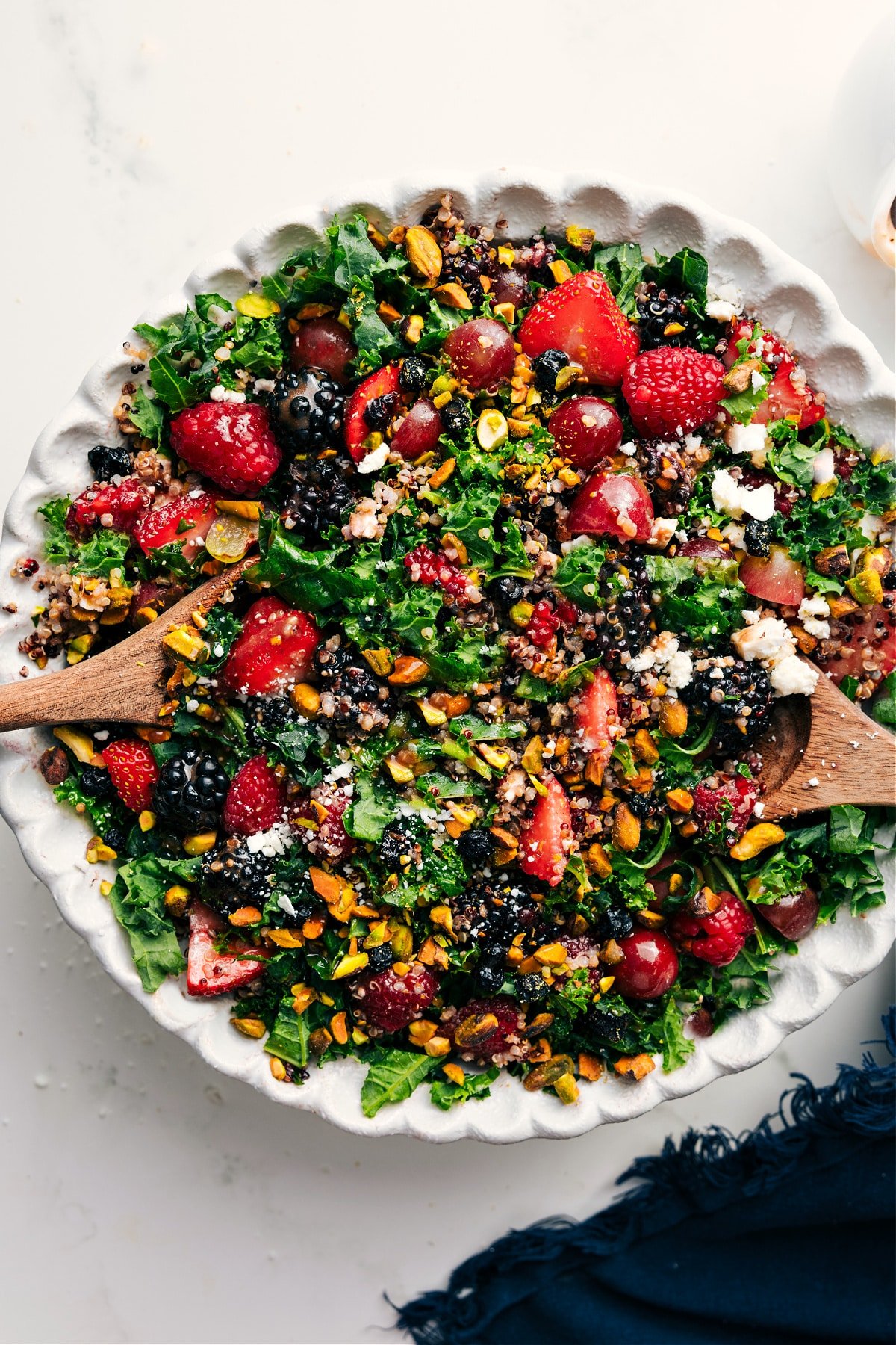 Kale And Quinoa Salad Recipe Tossed Together With Dressing Kale Quinoa Salad in a bowl with all the fresh mixings like berries, pistachios, and feta.