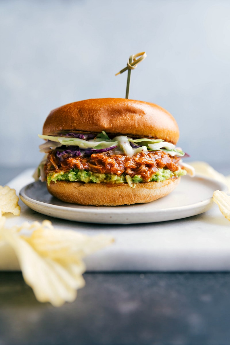 BBQ chicken sandwich with an abundance of BBQ chicken spilling out, served on a plate and ready to be eaten.