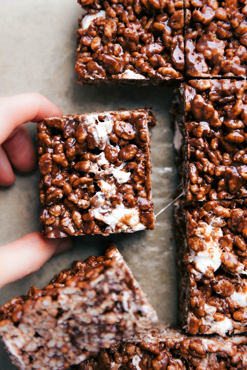 Chocolate rice krispie treats cut and being pulled apart to reveal its crunchy and gooey texture, a delicious twist on a favorite dessert.