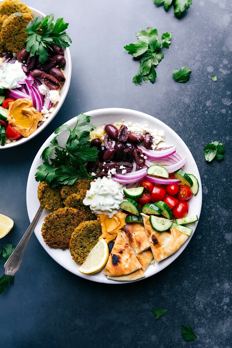 Baked falafel served on a plate with pita bread, tzatziki sauce, olives, onions, tomatoes, and cucumbers.