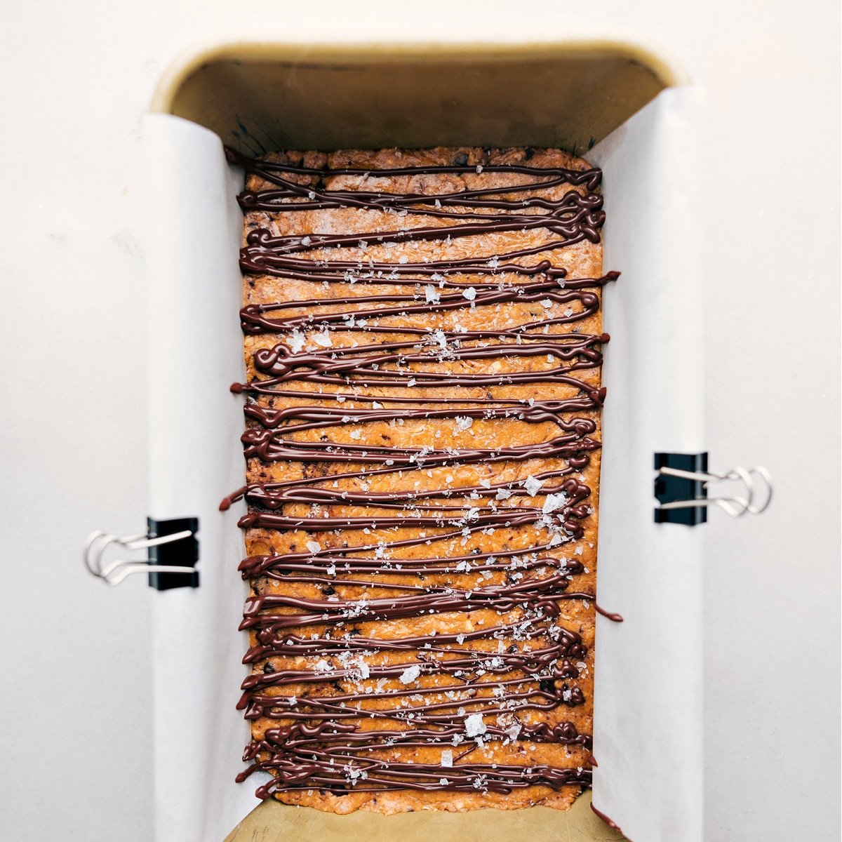 Chocolate being drizzled over the homemade protein bars and sea salt being sprinkled on top.