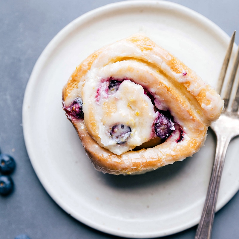 Image of one of the Lemon-Blueberry Sweet Rolls on a plate with a fork about to be eaten
