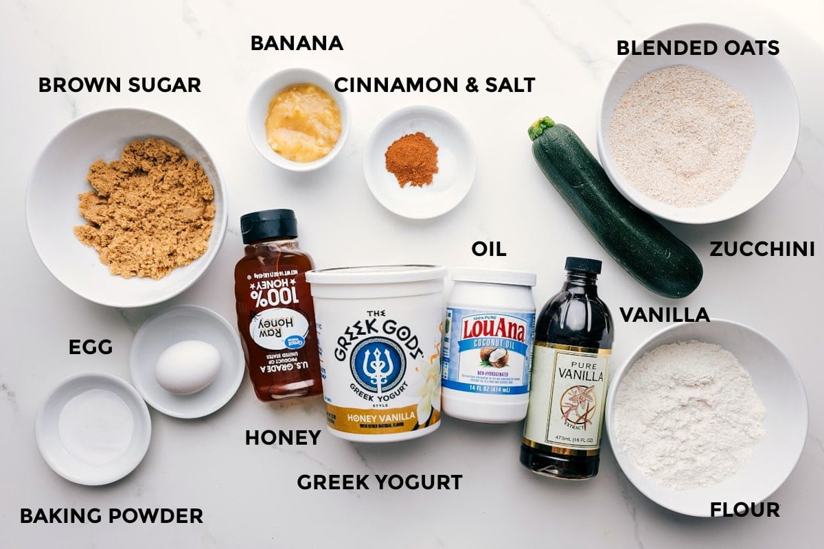 Ingredients In Banana Zucchini Muffins All the ingredients in this recipe prepped out for easy assembly including the brown sugar, egg, baking powder, honey, Greek yogurt, banana, cinnamon, salt, oil, vanilla, flour, zucchini, and blended oats.