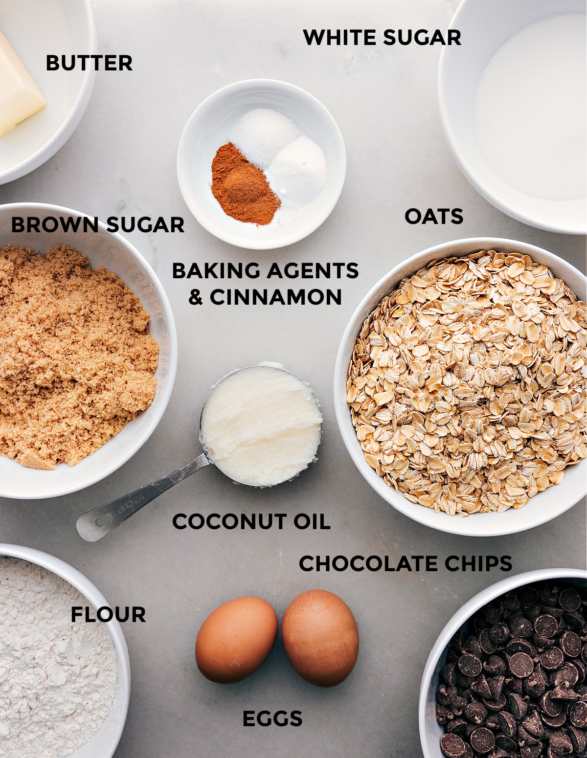 Ingredients for this recipe spread out such as oatmeal, sugar, eggs, spices, and chocolate chips.