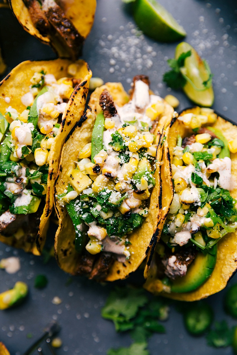 Finished steak taco recipe, with tacos side by side, stuffed with delicious meat, corn salsa, and various toppings.