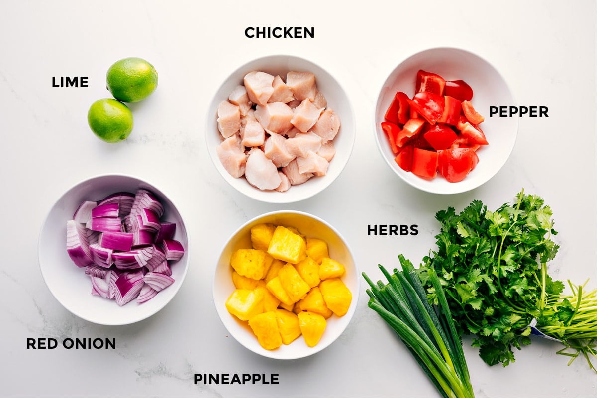 Ingredients In Teriyaki Chicken Skewers All the ingredient prepped out for easy assembly including the limes, red onion, pineapple, chicken, herbs, and pepper.