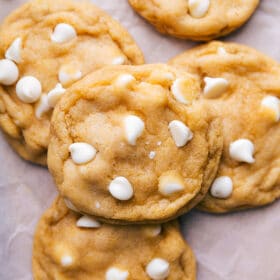 The completed recipe for cornmeal cookies, with white chocolate chips scattered around them, showcasing a warm and delectable treat.