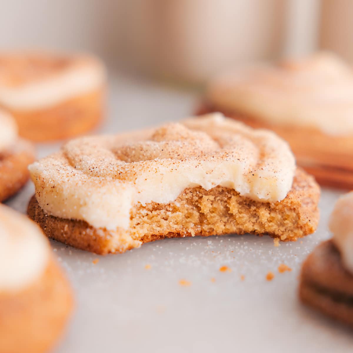 A cinnamon roll cookie topped with cream cheese frosting and cinnamon sugar, with a big bite missing.