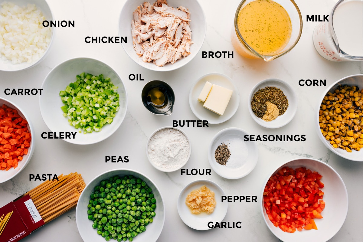 Prepped ingredients for creamy chicken noodle soup including onion, carrot, celery, pasta, peas, chicken, oil, butter, flour, garlic, seasonings, broth, milk, corn, and peppers.
